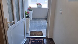 A narrow entrance with a glass door, a welcome mat, and potted plants on a balcony. - Belisima Delux - One Bedroom Apartment With Sea View (Rab)