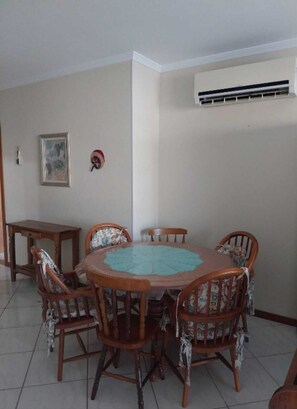 A dining area with a round wooden table and six chairs, a small side table, and a wall-mounted air conditioning unit.