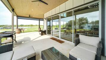 Un espace extérieur aménagé, abrité et doté de mobilier en osier, d’une table en verre et offrant une vue sur un terrain de golf.