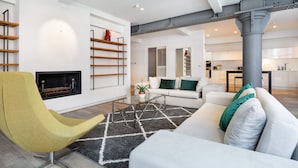 Un salon moderne avec un canapé, un fauteuil jaune, une cheminée et une cuisine en arrière-plan.