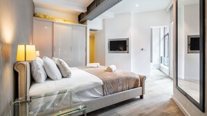 Une chambre moderne avec un grand lit, une table de chevet en verre, une armoire et un téléviseur fixé au mur.