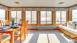 Una habitación con una mesa de comedor preparada para cuatro personas, un sofá y grandes ventanales con vistas al agua.