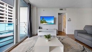 Ein modernes Wohnzimmer mit einem großen Fernseher, einem grauen Sofa und einem weißen Couchtisch mit einer Pflanze.