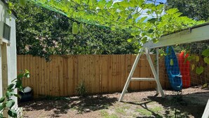 Un patio trasero con valla de madera, una escalera y plantas colgantes.