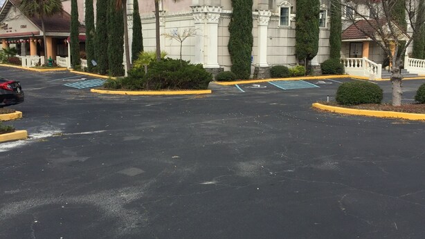 Un estacionamiento con un edificio de estilo arquitectónico clásico y altos cipreses.