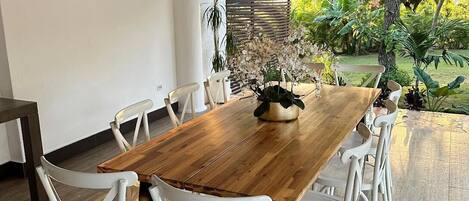 Un coin repas avec une table en bois et des chaises blanches, un ventilateur de plafond et une vue sur un jardin.