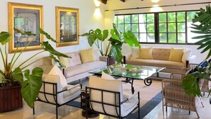 Un salón amplio con techo alto, ventanas grandes y una mezcla de muebles, incluyendo un sofá, sillones y una mesa de centro.