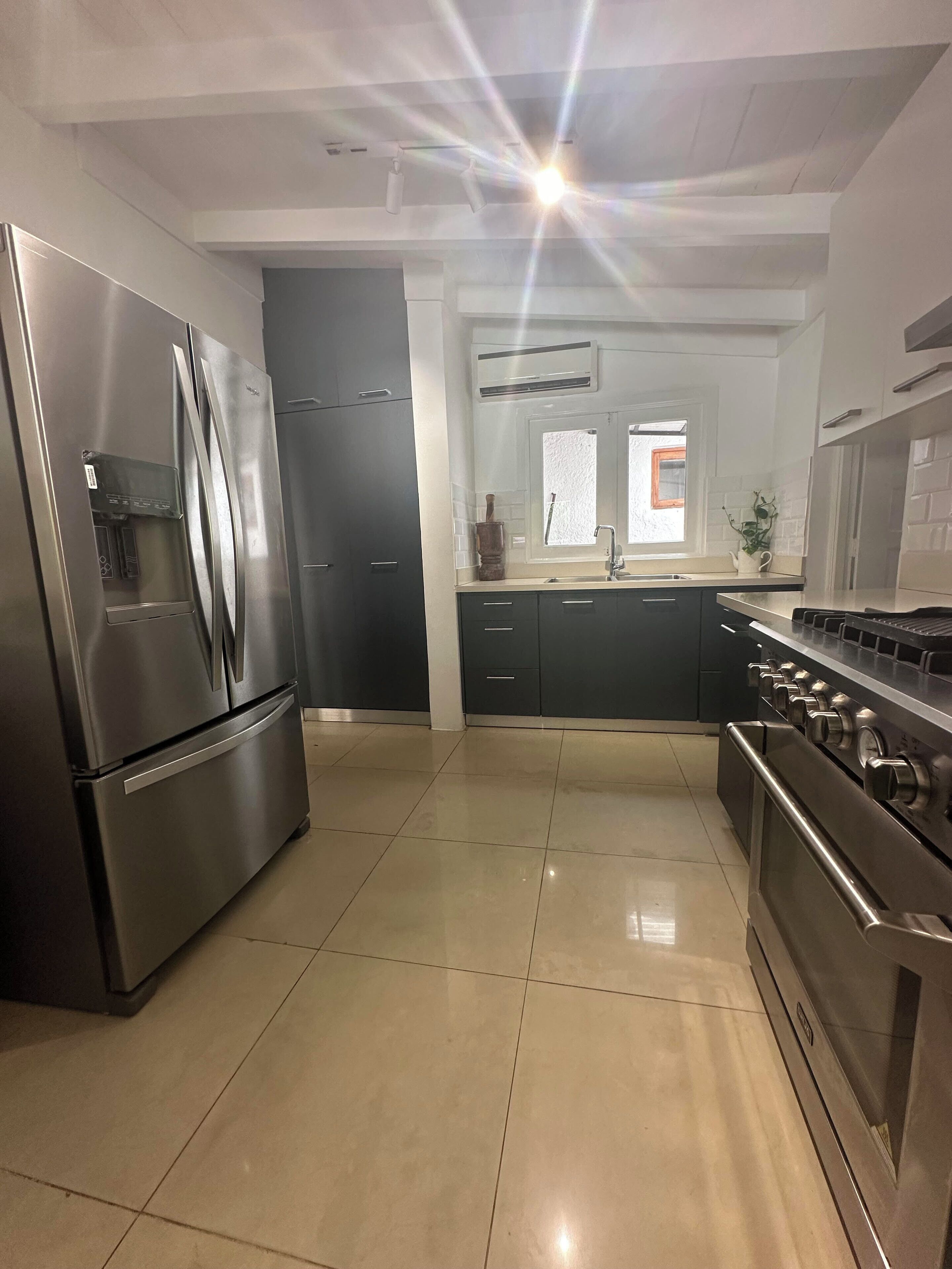 Una cocina moderna con electrodomésticos de acero inoxidable, piso de baldosas y un ventanal que proporciona luz natural.