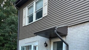 A two-story house with a grey siding exterior, a white door, and a small garden area with mulch and a few plants. - Alumni Corner

 (State College)