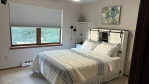 A bedroom with a bed, a ceiling fan, a window with blinds, a nightstand, a lamp, and a wall art piece. - Alumni Corner

 (State College)