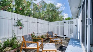 A patio with two wooden chairs, a white fence, and a door. - Beach Bliss by 7M Beach (West Bay)