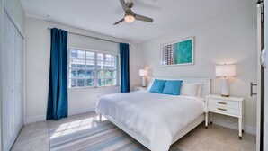 A bedroom with a bed, nightstands, a ceiling fan, a window with curtains, and a painting on the wall. - Beach Bliss by 7M Beach (West Bay)