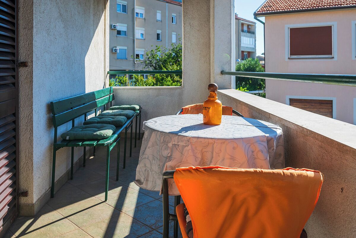 Un balcon avec une table ronde, des chaises vertes et une chaise orange.