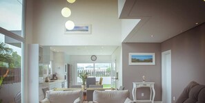 A modern living room with a sofa, a small table, and a view through a glass door to an outdoor area. - Rosa Internacional - Surfland (Garopaba)