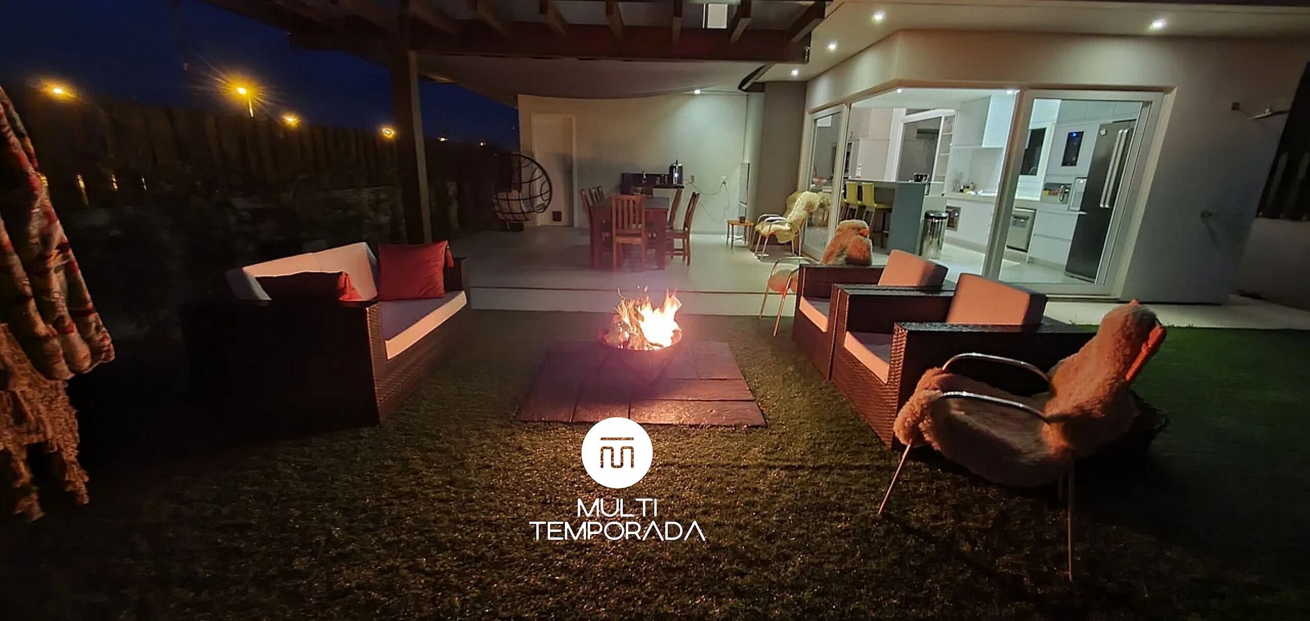 Un patio al aire libre con una chimenea, asientos y vistas al interior de la casa.