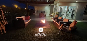 An outdoor patio with a fire feature, seating, and a view into the house.