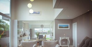 A modern living room with a sofa, a small table, and a view of the outdoors through a glass door. - Rosa Internacional - Surfland (Garopaba)