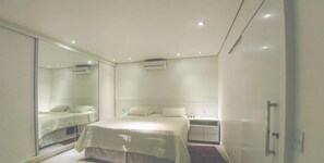 A modern bedroom with a large bed, a bedside table, a wardrobe, and a mirror. - Rosa Internacional - Surfland (Garopaba)
