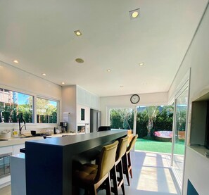 A modern kitchen with a bar area, large windows, and a view of the backyard. - Rosa Internacional - Surfland (Garopaba)