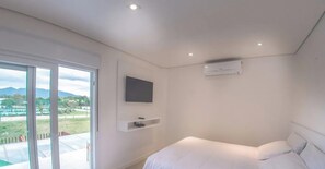 A modern hotel room with a large window, a flat-screen TV mounted on the wall, and a bed with white bedding.