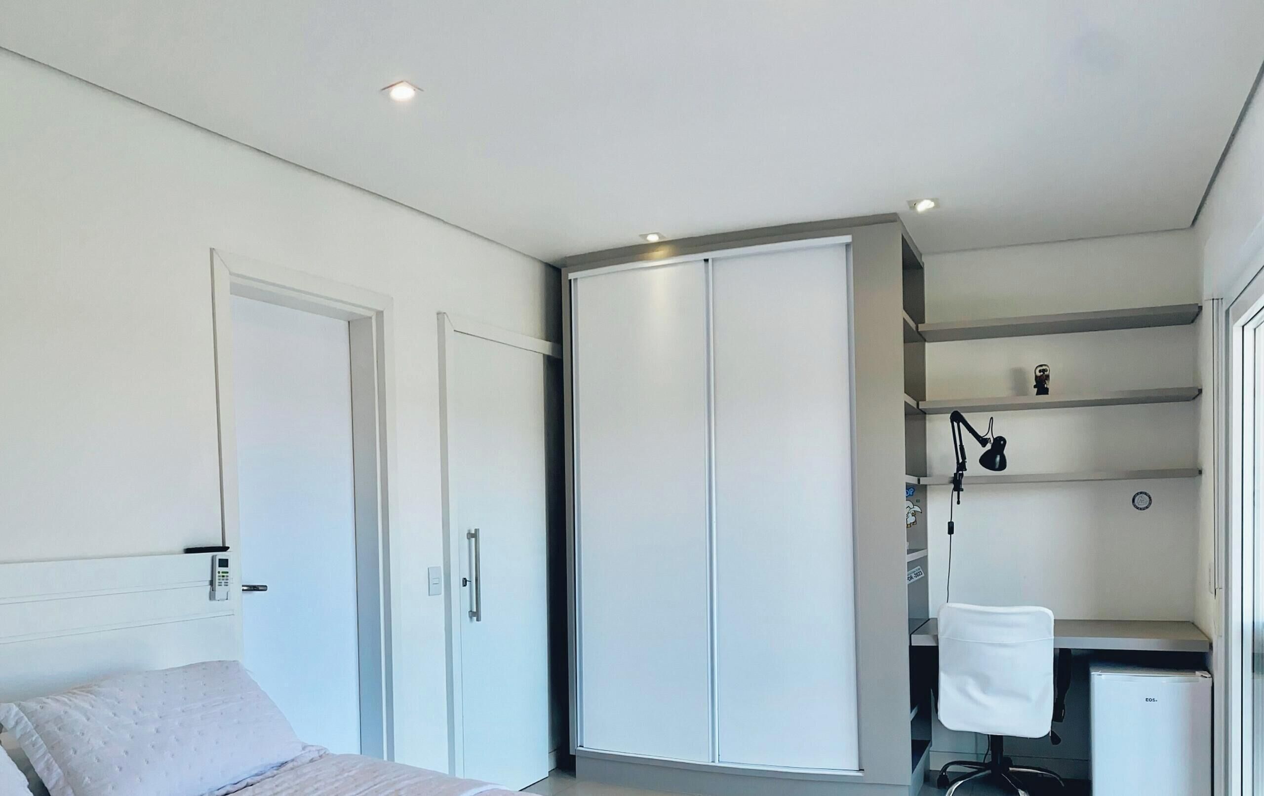 Un dormitorio con cama, armario y escritorio con silla.