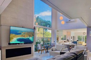 A modern living room with a large TV, comfortable seating, and a view of the outdoors.