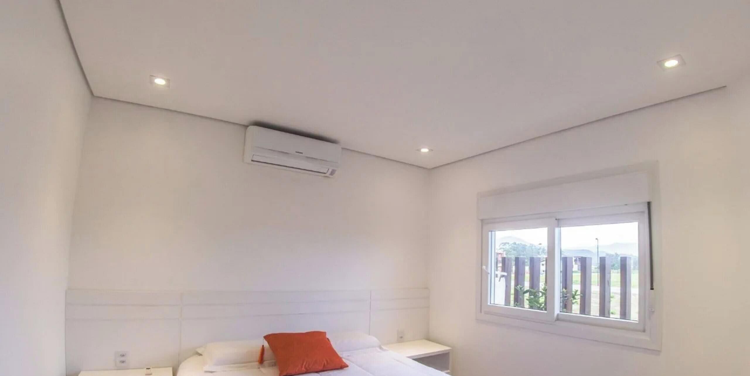 A bedroom with a bed, an air conditioning unit, a window with a view, and a white ceiling.