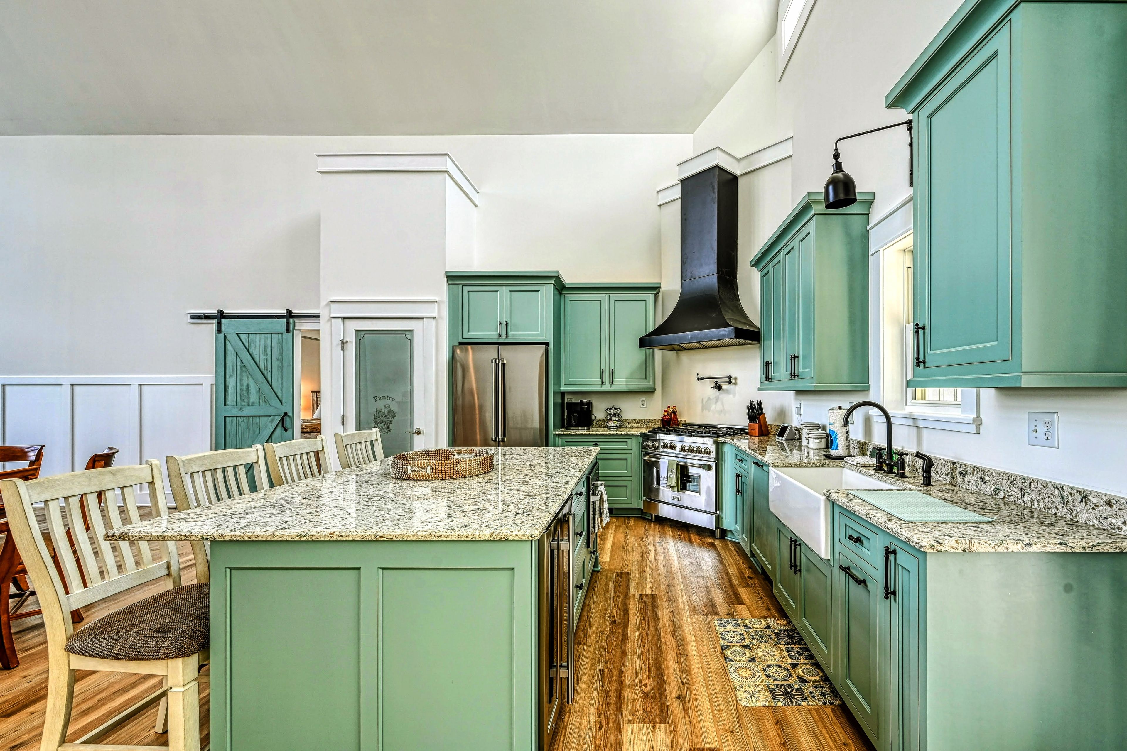 A kitchen with a central island, green cabinets, stainless steel appliances, and a wooden floor.