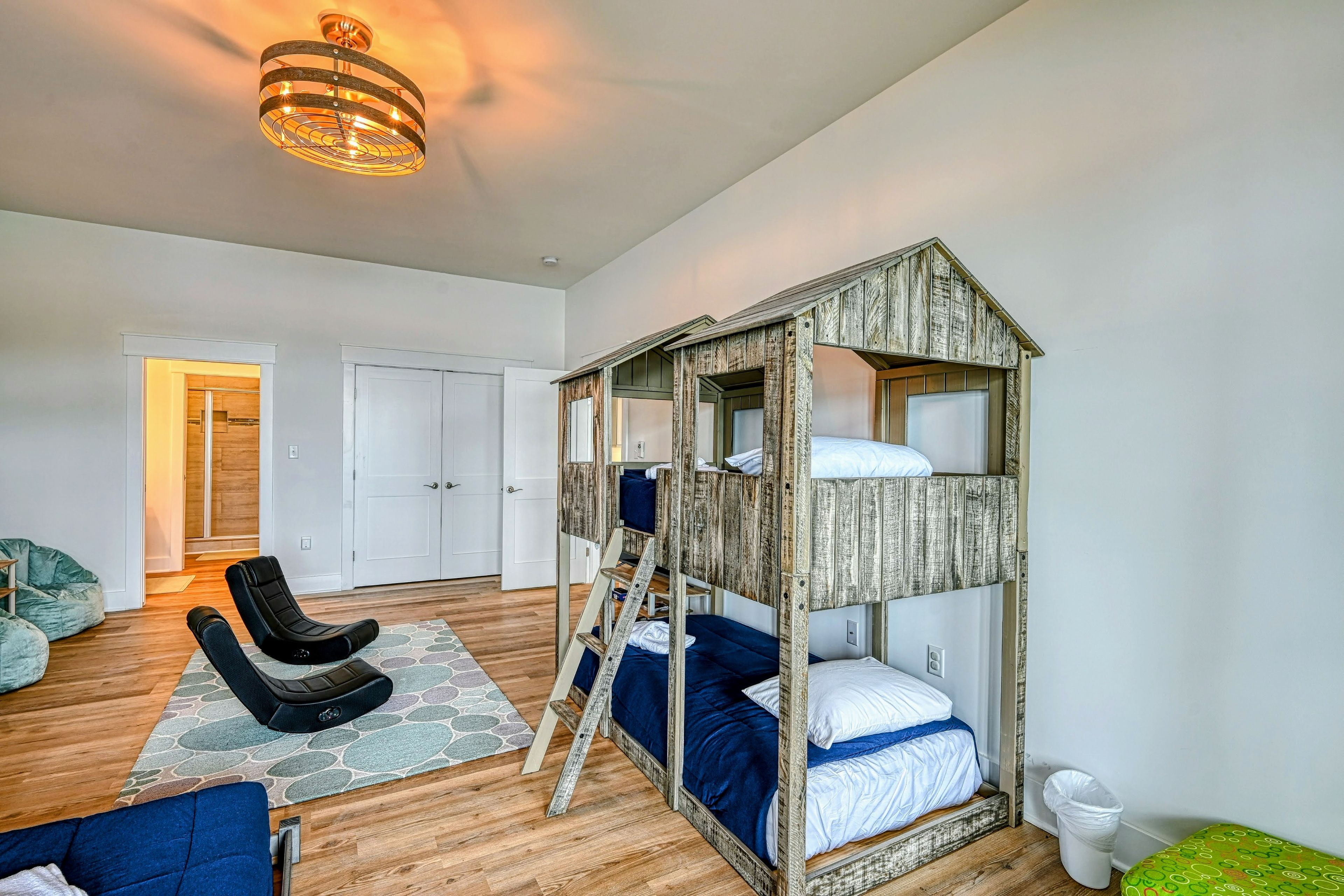 A room with a bunk bed, a chair, a desk, and a hanging light fixture.