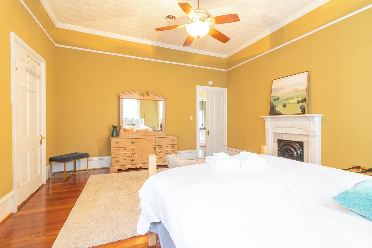 A bedroom with a bed, dresser, bench, and a fireplace.