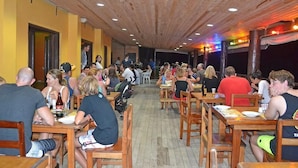 A restaurant with wooden tables and chairs, yellow walls, and a wooden ceiling. - Ratu Kini's Dive & Stay (Mana Island)