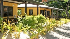 A yellow building with a covered outdoor area and a sandy ground. - Ratu Kini's Dive & Stay (Mana Island)
