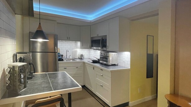 A modern kitchen with white cabinets, stainless steel appliances, and a dining area with a table and chairs. - Great Mid-Town Toronto Bachelor Suite Convenient to Downtown and Airport (Toronto)