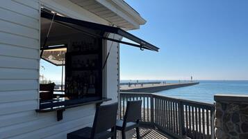 A bar area with a view of the ocean, a stone wall, and a wooden deck with chairs.