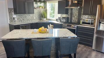 A modern kitchen with dark cabinets, a large island with bar stools, a stove, microwave, and refrigerator.