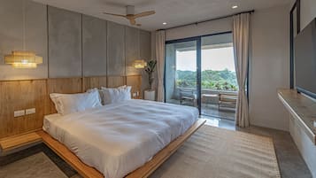 Un dormitorio moderno con una cama grande, cabecera de madera, ventilador de techo y vistas al exterior a través de un ventanal corredero.
