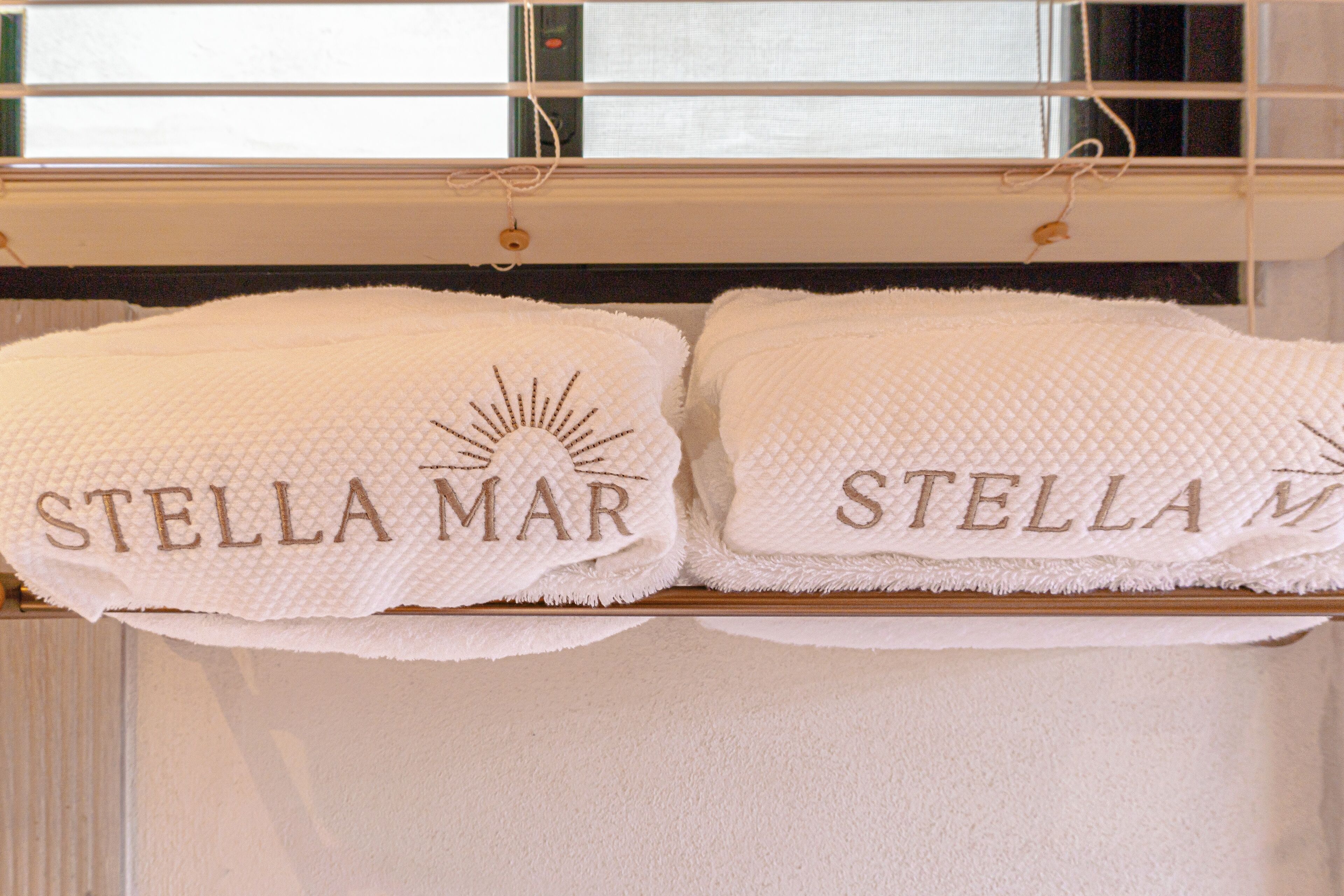 Two white towels with "STELLA MAR" embroidered on them hanging on a rack.