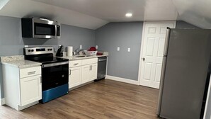 Una cocina con armarios blancos, un microondas de acero inoxidable, una estufa negra y un refrigerador gris.