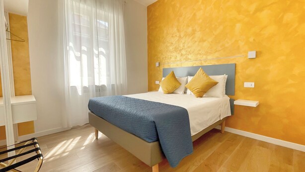 Quarto de hotel com cama, mesa de cabeceira, cadeira e janela com cortinas.