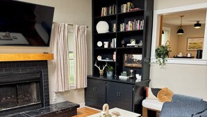 Una sala de estar con chimenea, una estantería negra, un sofá gris y un televisor de pantalla plana.