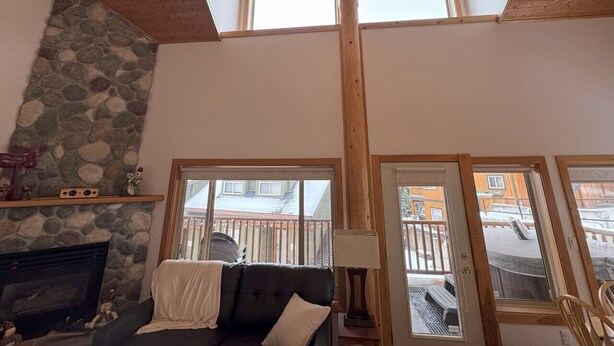 A living room with a stone fireplace, a couch, and a skylight. - Apex Mountain ~ Ubuntu at Apex (Keremeos)