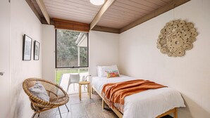 Een slaapkamer met een bed, een rieten stoel, een raam en een decoratief wandobject.