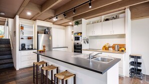 Een moderne keuken met een centraal eiland, ingebouwde apparaten en een trap naar een hoger niveau.