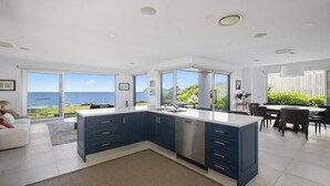 Cocina moderna con vista al mar, que incluye una isla grande, armarios azul oscuro y un comedor con vistas.