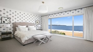 Un dormitorio con una cama grande, una mesita de noche, una lámpara y vista a la playa.