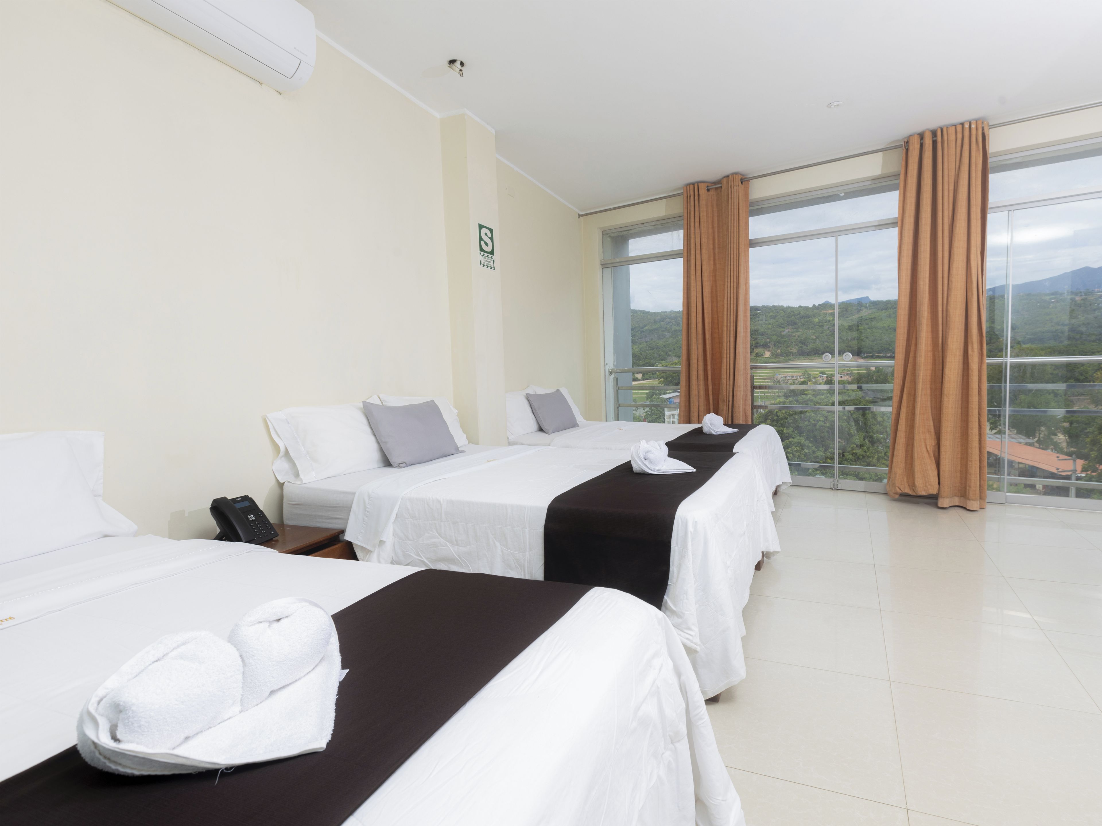 A hotel room with two beds, a phone on the nightstand, and a view of the landscape through large windows.