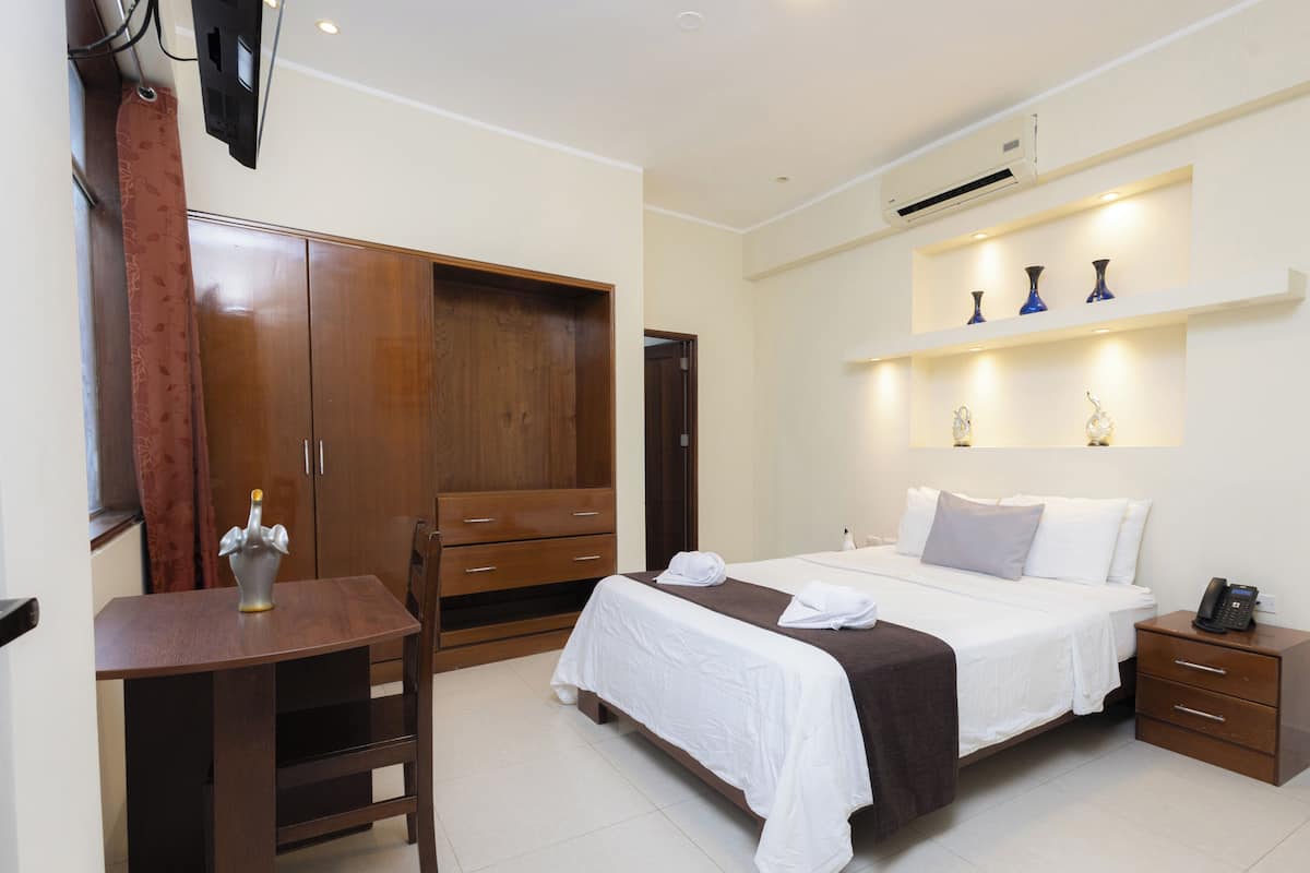 Una habitación de hotel con cama, mesita de noche, silla, armario y escritorio.