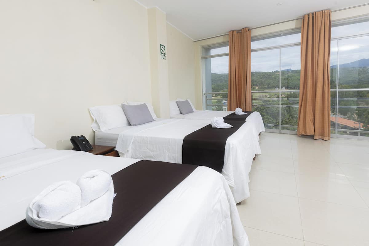 Habitación de hotel con dos camas, un teléfono en la mesita de noche y vista al paisaje a través de amplias ventanas.