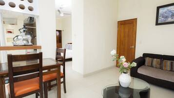 A living room with a sofa, a dining table with chairs, a coffee table with a vase, and a wooden door.