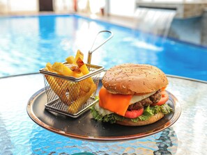 Una mesa de comedor con una hamburguesa y una cesta de papas fritas cerca de una piscina.